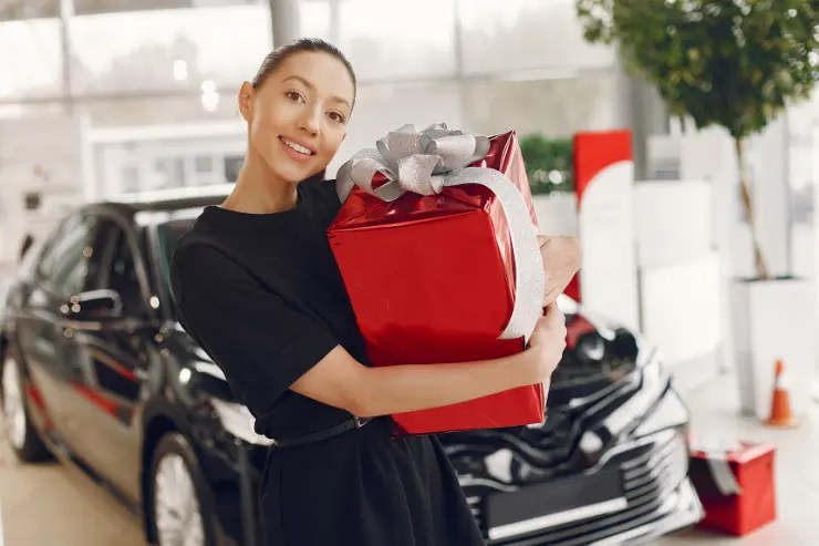 mujer-con-regalo Vendedora en un concesionario de coches con un regalo rojo